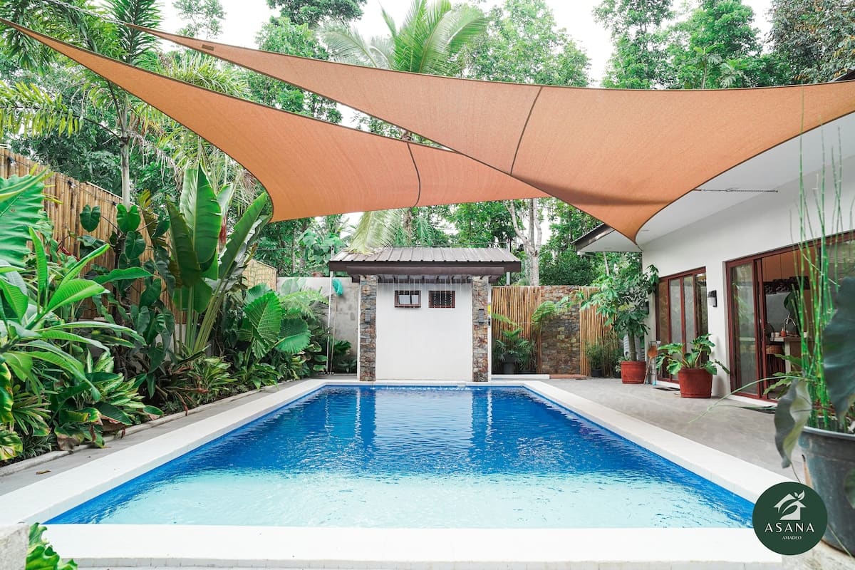 Private swimming pool shaded by a large triangular sail, surrounded by tropical greenery
